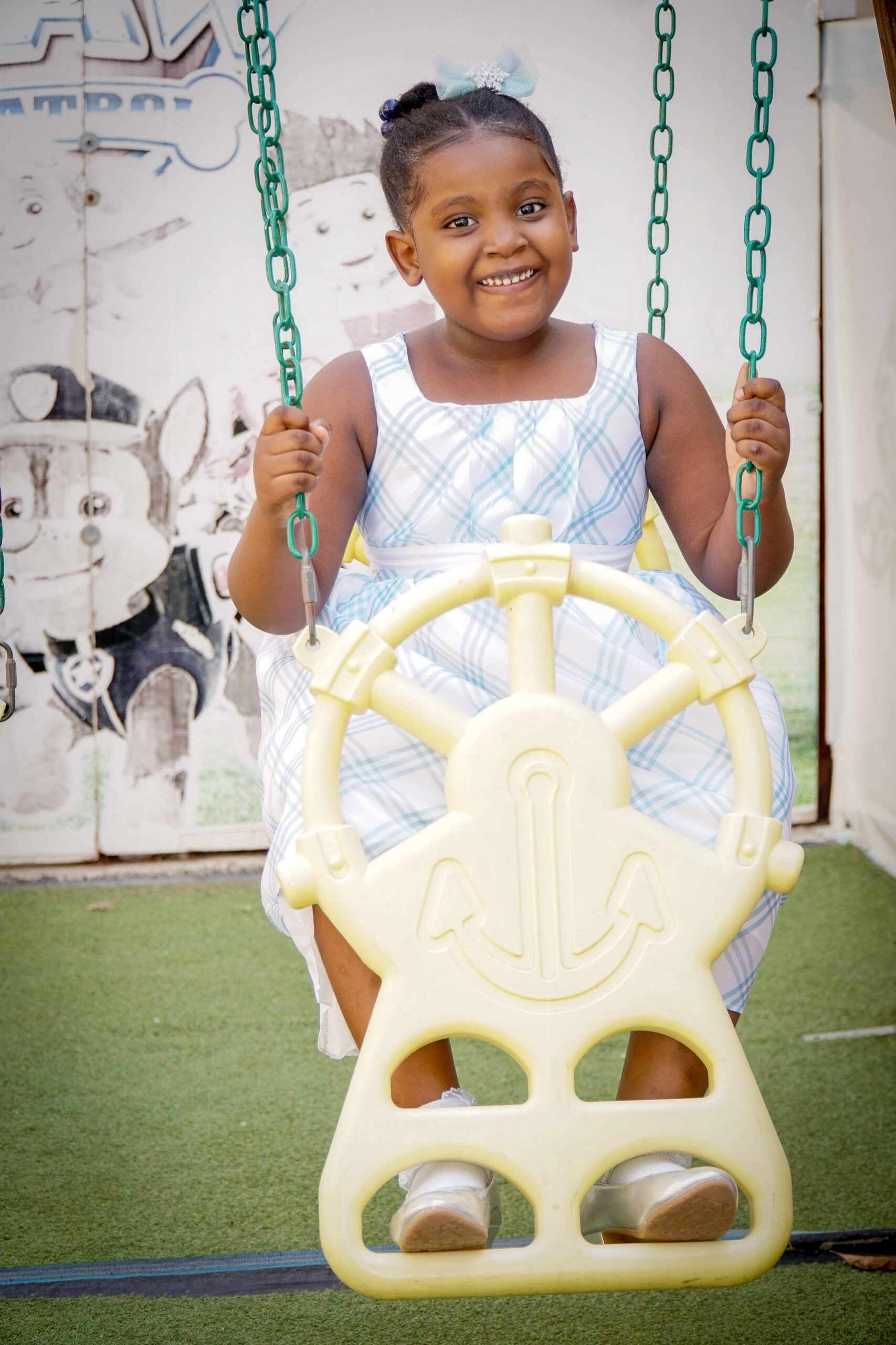 Smiling preschool girl on a playground swing at Better Life Club Haiti