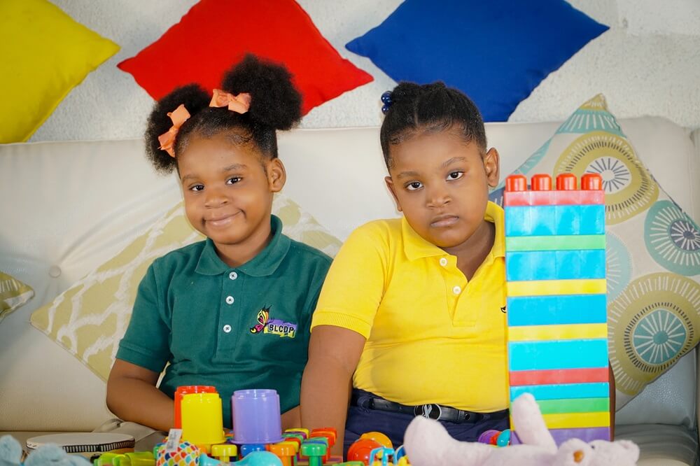 Two young girls sitting beside colorful educational blocks at Better Life Club Haiti